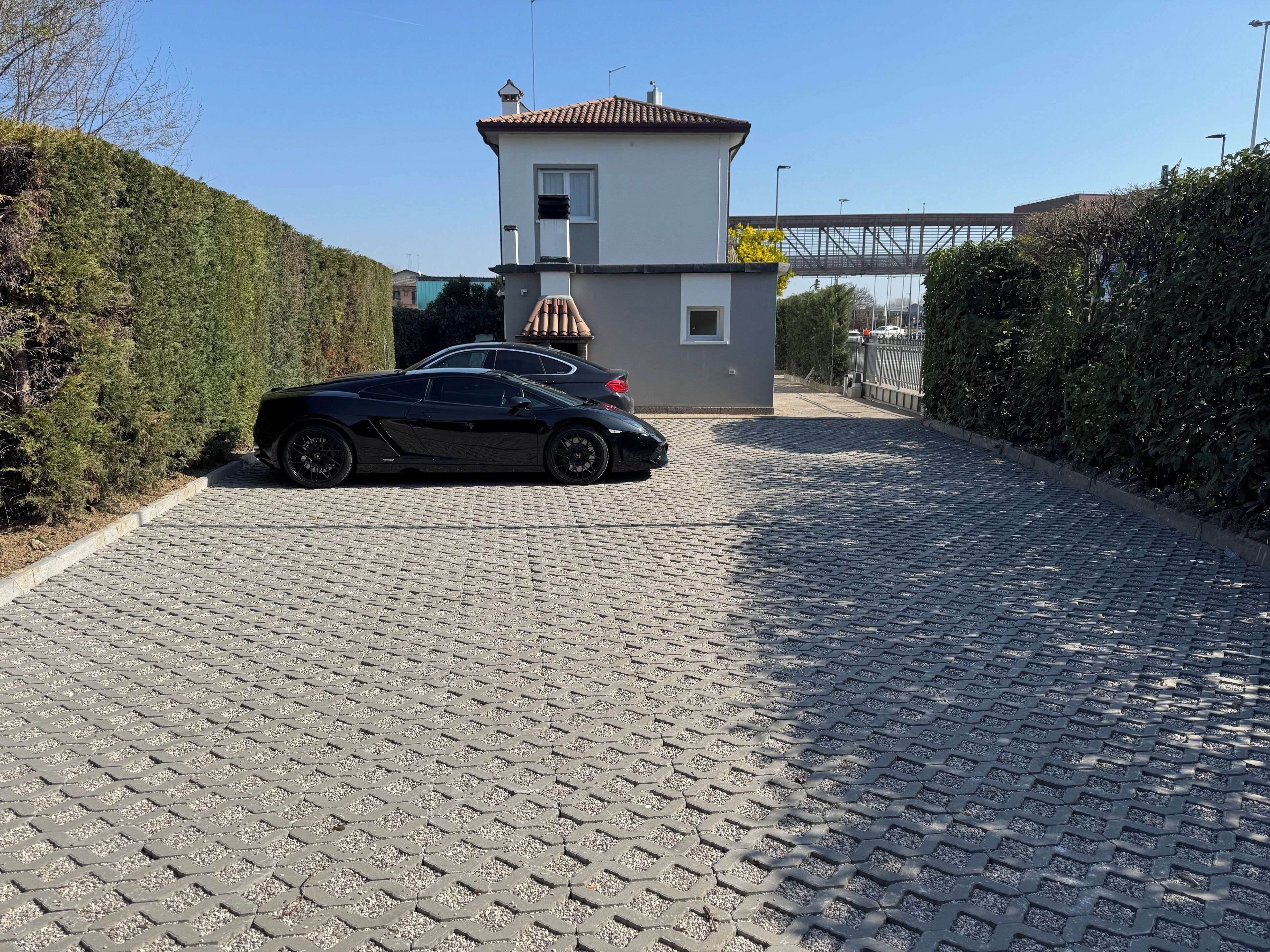 Un'auto nera parcheggiata su un vialetto in pietra che conduce a una casa con una piccola struttura simile a una torre.