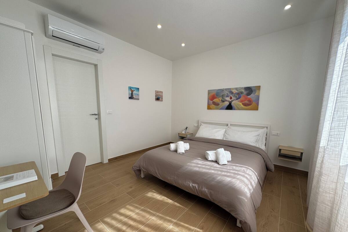 Ein Hotelzimmer mit Bett, Sessel, Schreibtisch, Klimaanlage und einem Bild an der Wand.