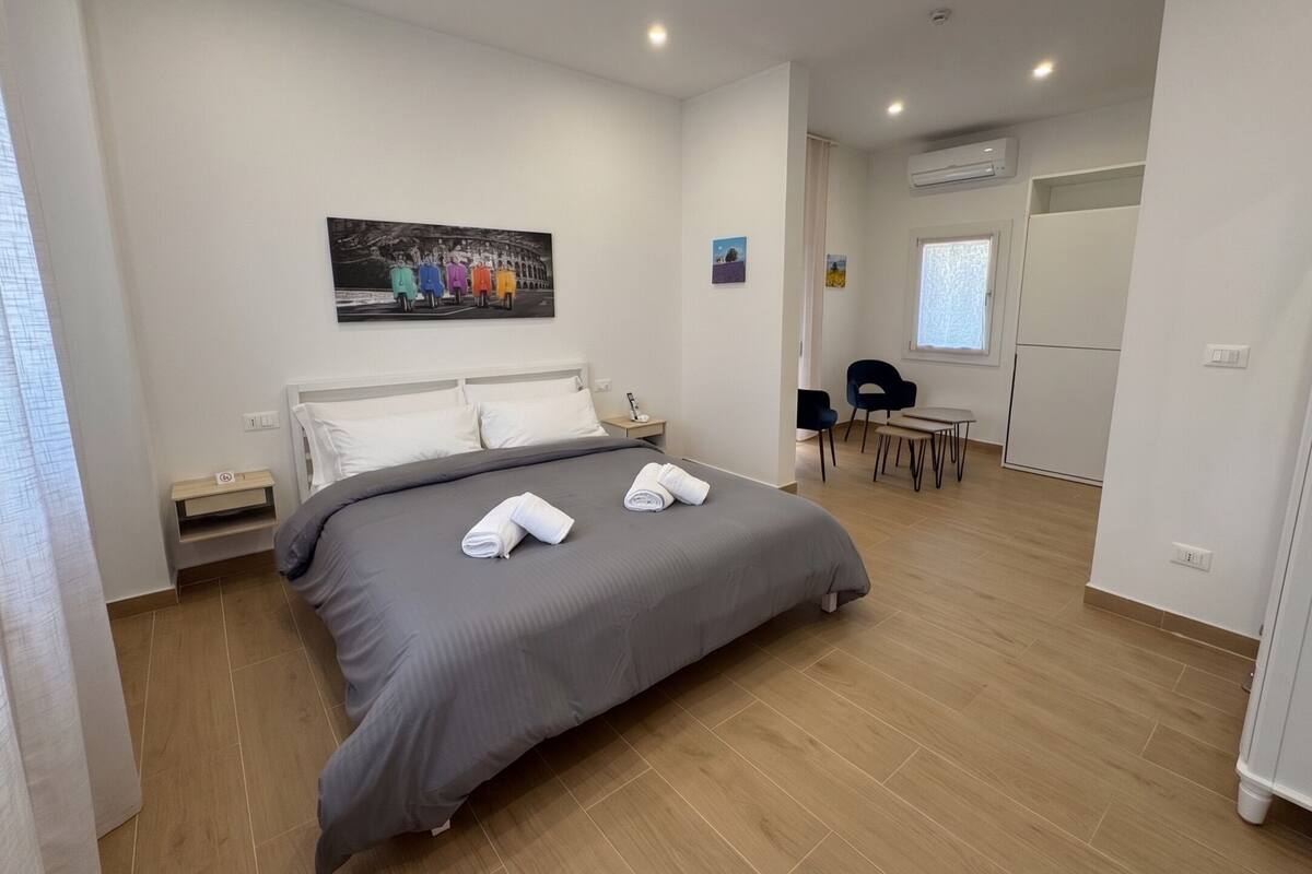 Ein modernes Hotelzimmer mit einem großen Bett, einem kleinen Schreibtisch, einem Sessel und einem Esstisch.