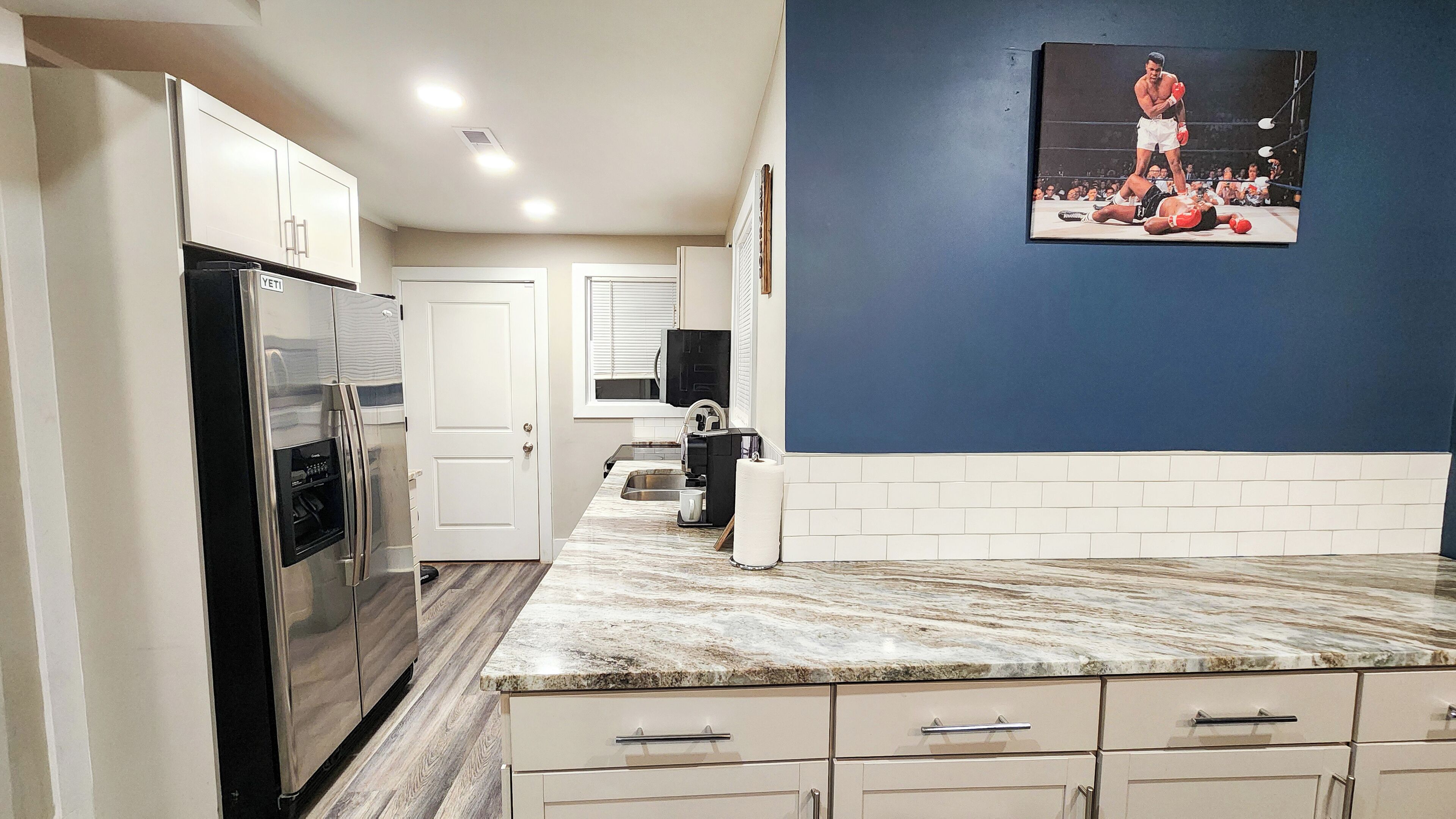 A kitchen with a marble countertop, stainless steel refrigerator, and white cabinets.