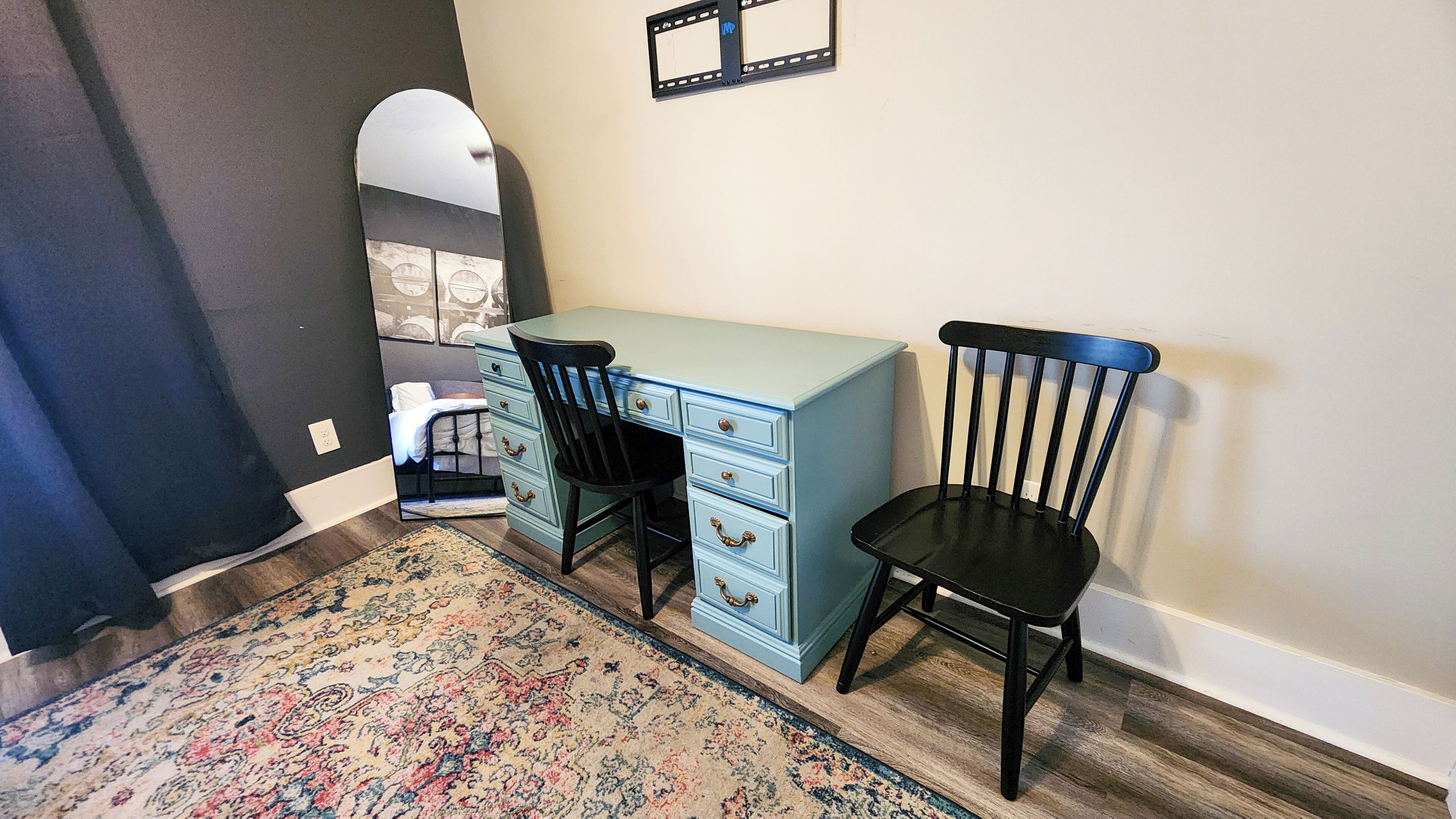 A room with a blue desk, black chair, and a patterned rug.