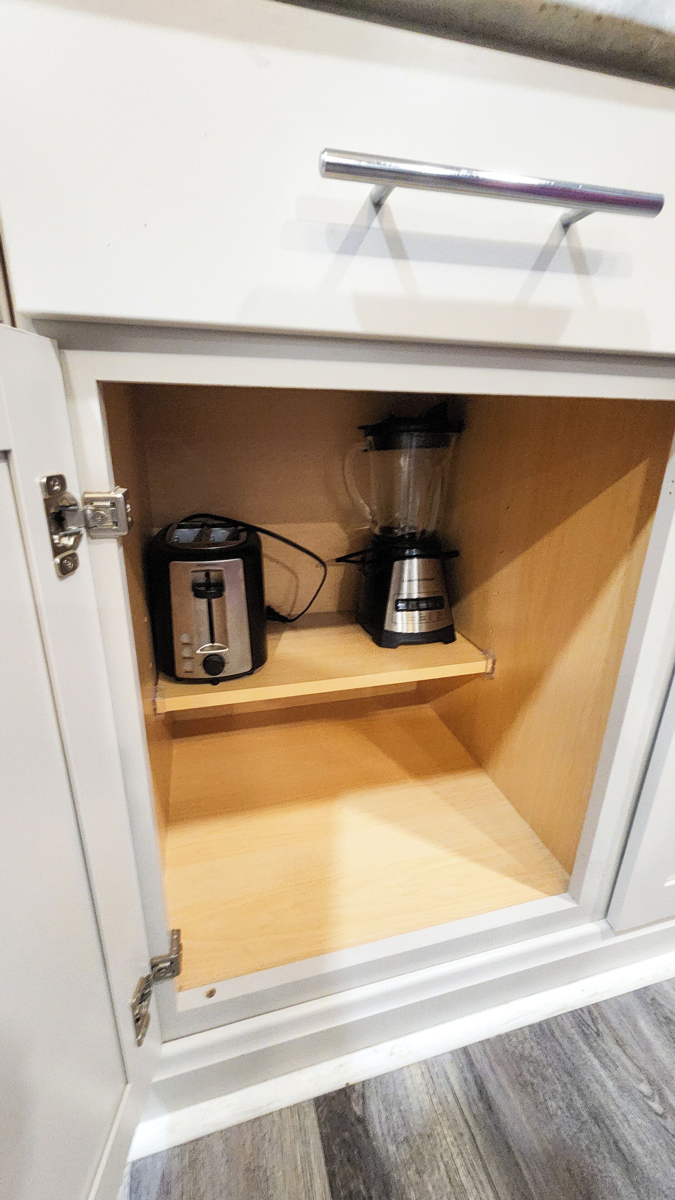 A kitchen cabinet with a toaster and a blender on a shelf.
