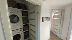 A laundry room with two washing machines, storage baskets, and a hallway leading to another room. - Modern Living with Rooftop Views (Pittsburgh)
