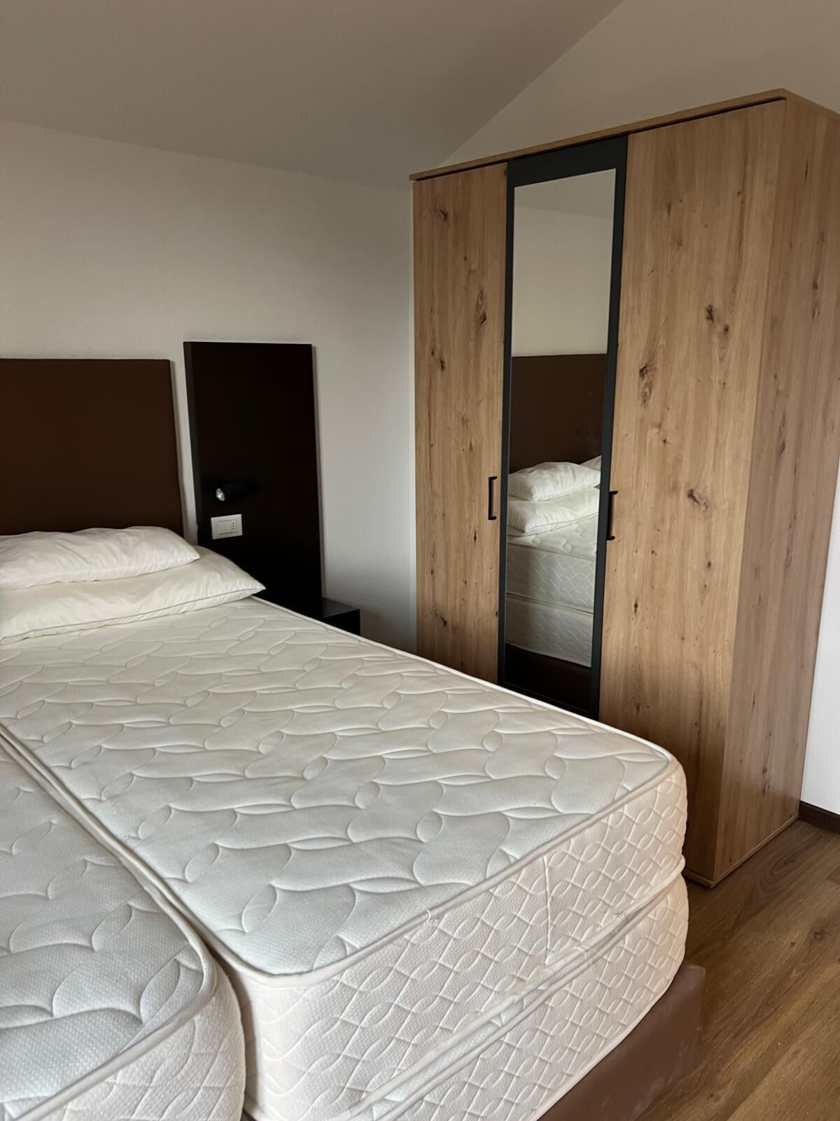 Een slaapkamer met een groot bed, een houten garderobe en een nachtkastje.