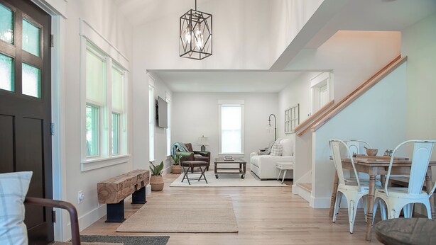 A spacious living room with a large window, a wooden bench, a sofa, a dining table with chairs, and a staircase. - Pure Blue on M22 in Northport Village (Northport)