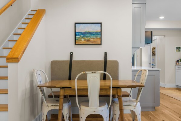 Un comedor con mesa de madera y sillas blancas, un sofá color beige y un cuadro en la pared.