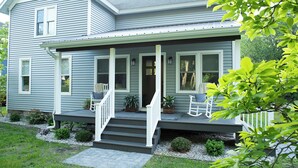 A two-story house with a front porch, steps, and a small garden area with plants and a bench. - Pure Blue on M22 in Northport Village (Northport)