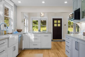 A modern kitchen with white cabinetry, a central island, and a view of the outdoors through large windows.