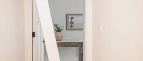 A hallway with a white door, a small desk with a plant, and a framed picture on the wall.