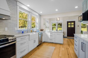 A modern kitchen with white cabinetry, a stainless steel stove, and a large window providing natural light.