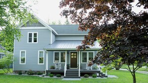A two-story house with a front porch, a covered entryway, and a small front yard with a tree and shrubs. - Pure Blue on M22 in Northport Village (Northport)