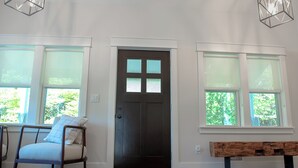 A room with a dark wooden door, two windows with blinds, a wooden bench, and a chair with a cushion. - Pure Blue on M22 in Northport Village (Northport)