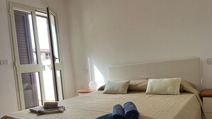 Een net opgemaakt bed met een beige deken, twee kussens en opgerolde handdoeken op het bed.