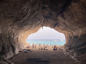 A beach scene viewed through a cave entrance with boats on the water and people on the sand. - Casa vacanze spaziosa , perfetta per famiglie (OROSEI)