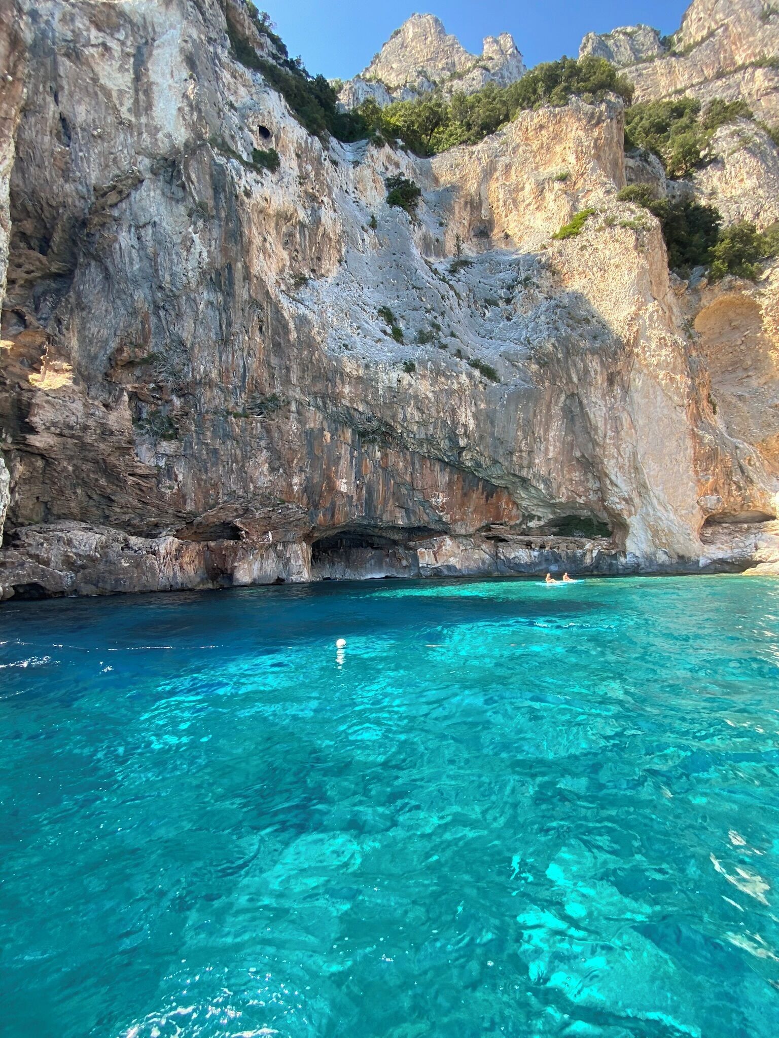 Litoral rochoso com águas turquesa límpidas e a entrada de uma gruta.