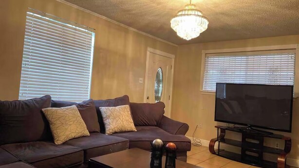 A living room with a brown sectional sofa, a flat-screen TV on a wooden stand, and a chandelier.