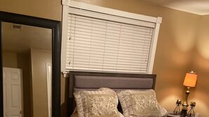 A bedroom with a bed, a mirror, a lamp, and a door.