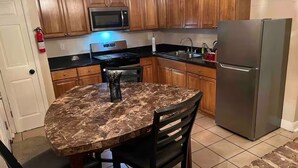 A kitchen with wooden cabinets, a stainless steel refrigerator, a microwave, and a dining table with chairs.