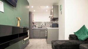 Eine moderne Küche mit grauen Schränken, einer schwarzen Arbeitsplatte und einer Mikrowelle. Auf einem dunklen Sofa liegt ein grünes Kissen und an der Wand steht eine Giraffenfigur.