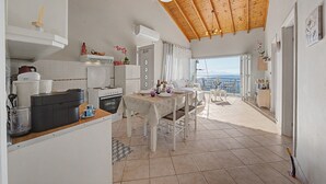 A spacious kitchen with a dining area, wooden ceiling, and a view of the sea. - Dorothea Apartment in Chlomos with Sea View, Wi-Fi and Air Conditioning (Χλομός)