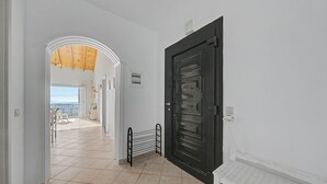 A hallway with a black door, a white bench, and a view of the sea through an open archway. - Dorothea Apartment in Chlomos with Sea View, Wi-Fi and Air Conditioning (Χλομός)