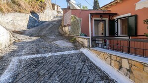 A narrow, cobblestone street with a steep incline, a stone wall on one side, and a building with a red facade and a black metal railing. - Dorothea Apartment in Chlomos with Sea View, Wi-Fi and Air Conditioning (Χλομός)