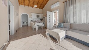 A spacious living area with a high wooden ceiling, a sofa, a dining table, and a kitchen in the background. - Dorothea Apartment in Chlomos with Sea View, Wi-Fi and Air Conditioning (Χλομός)