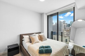 A modern hotel room with a large window, a bed with multiple pillows, a bedside table, and a mirror. - New 1BR+Den | Rooftop Deck |Free Parking (Miami)