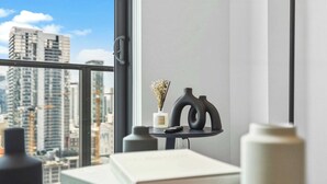 A room with a view of tall buildings, a small table with a vase and a book, and a window with a handle. - New 1BR+Den | Rooftop Deck |Free Parking (Miami)