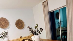Un coin repas avec une table en bois, des chaises en osier et deux vases blancs ornés de plantes.