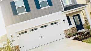 Une maison moderne à deux étages, dotée d’un garage, d’une porte d’entrée et d’un petit jardin.