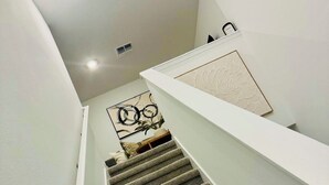 Un escalier dont les marches sont recouvertes de moquette, menant à un palier orné d’un panneau décoratif et d’un tableau encadré.