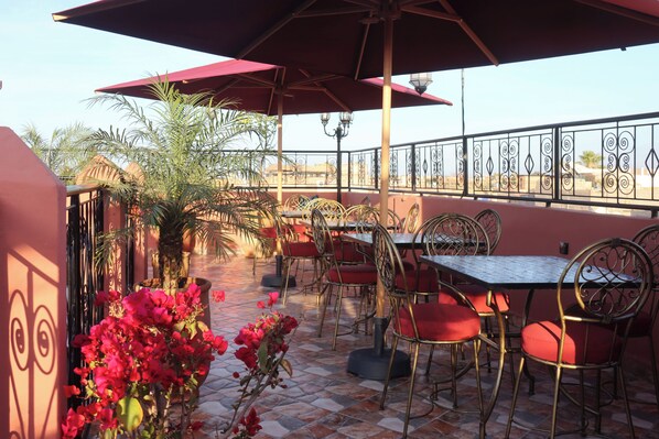 An outdoor patio with tables and chairs, a tiled floor, and a view of buildings in the background. - Riad Atlas Mejbar ( Adults Only) (Marrakech)