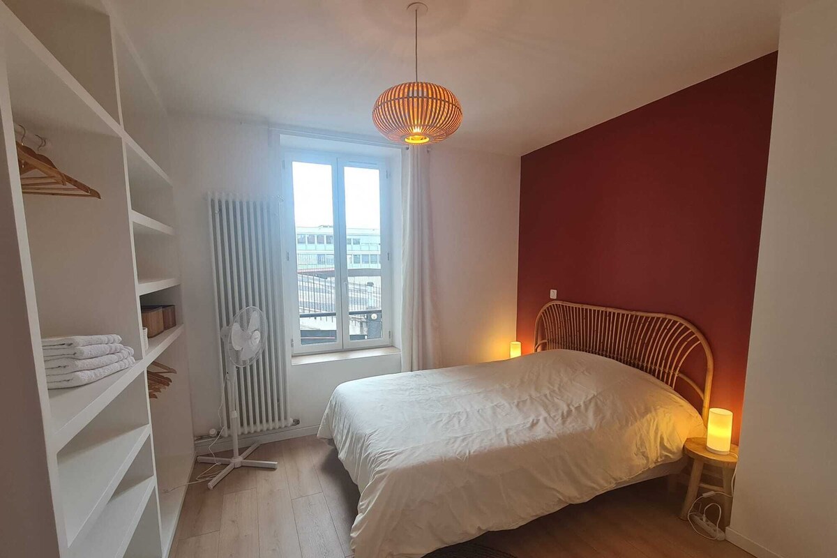 A bedroom with a bed, a radiator, a window, a fan, and a hanging light fixture.