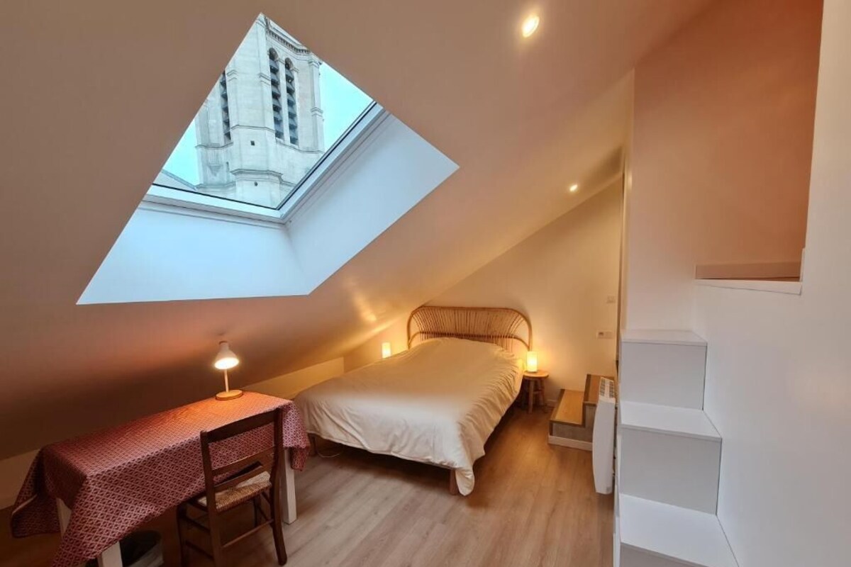 A bedroom with a skylight, a bed, a desk, and a staircase.