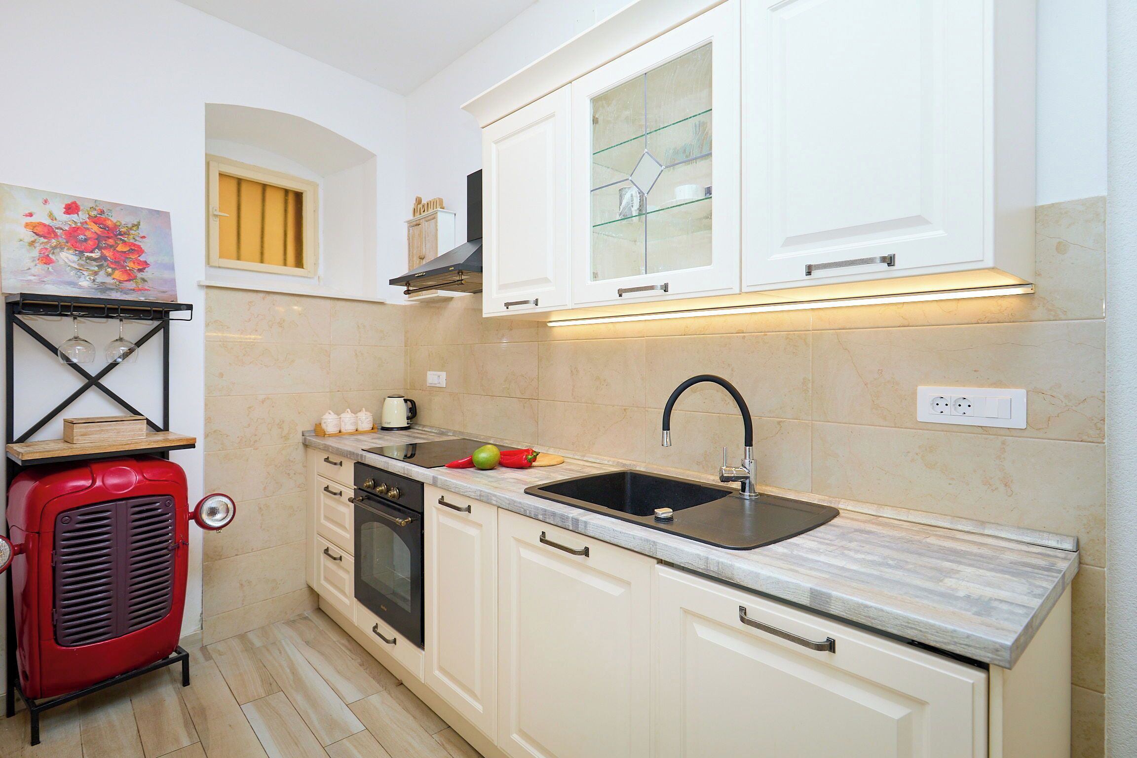A compact kitchen with white cabinets, a black sink, a red vintage stove, and a small window with yellow blinds.