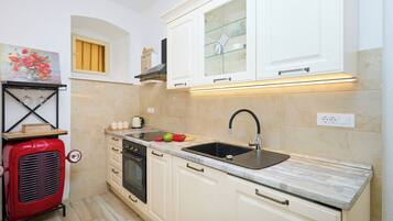 A compact kitchen with white cabinets, a black sink, a red vintage stove, and a small window with yellow blinds.