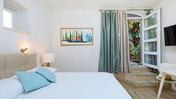 A bedroom with a bed, a nightstand, a lamp, a painting, a window, and a door leading to a balcony.