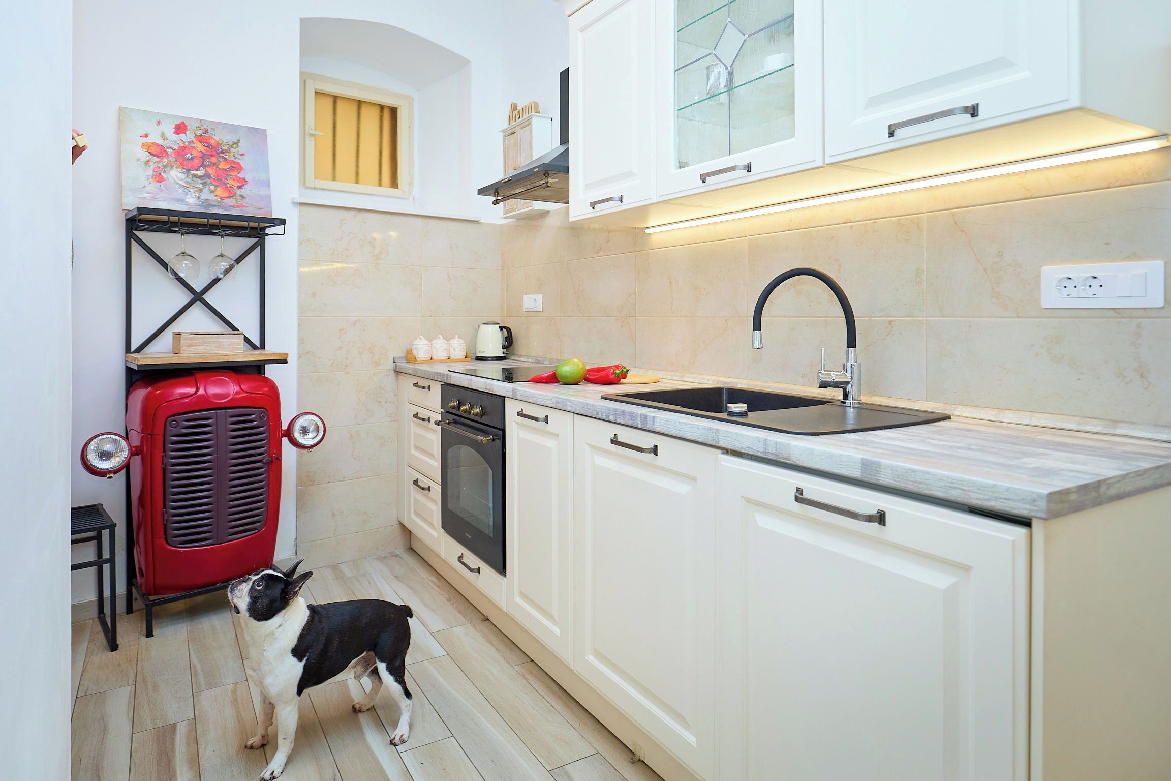 A kitchen with white cabinets, a red vintage stove, a sink, and a dog.