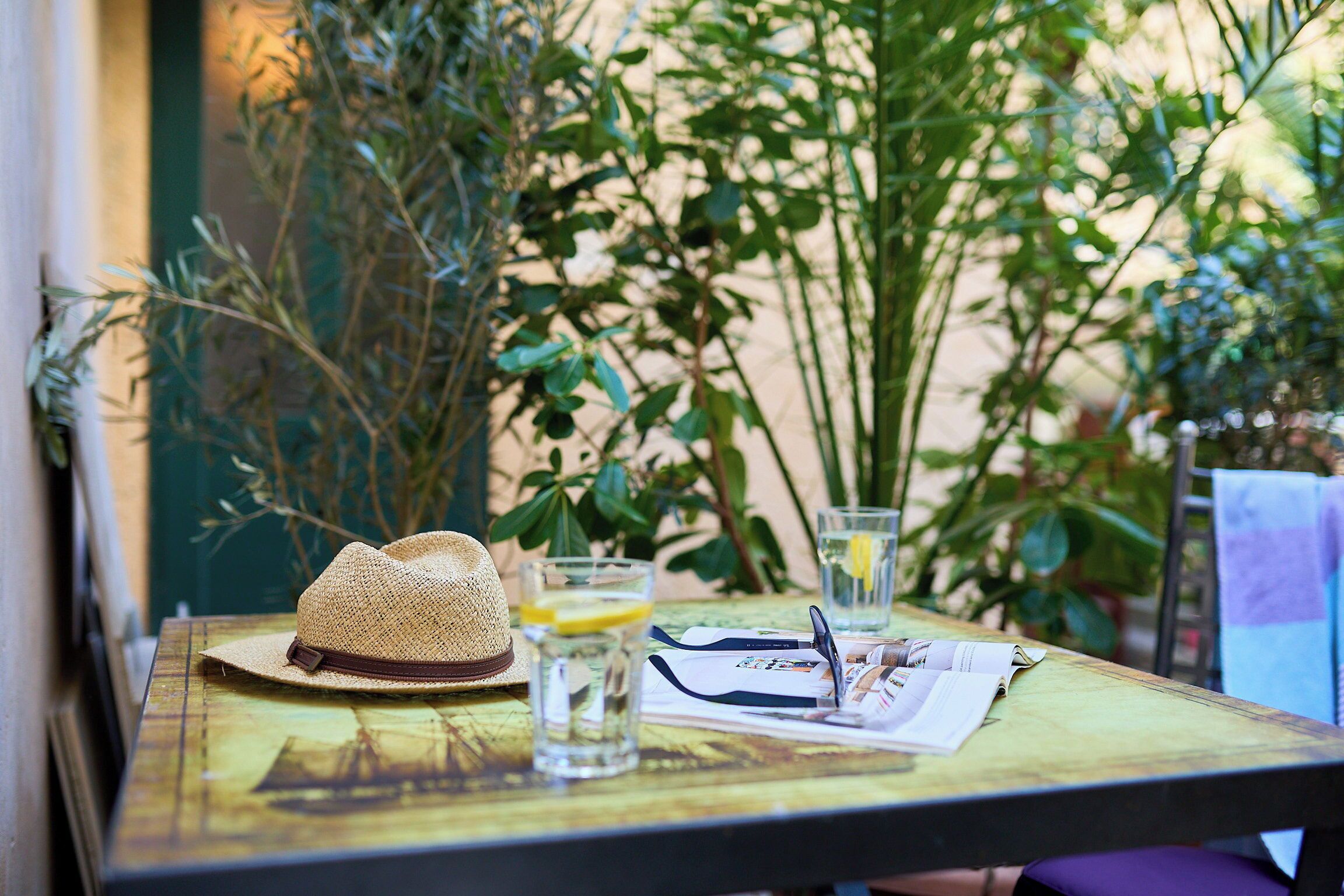 A table with a straw hat, glasses, a newspaper, and a glass of water.