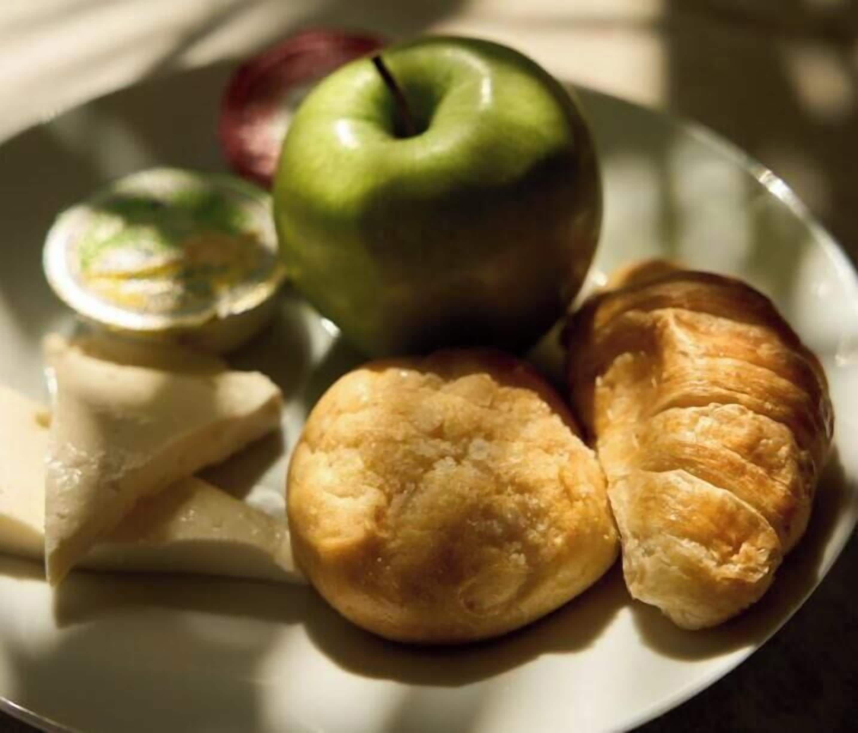 A plate with a green apple, a pastry, and a cheese slice.