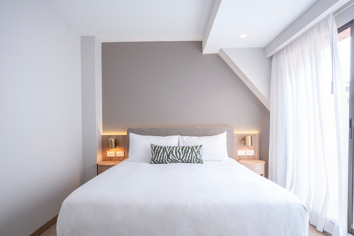 Une chambre d’hôtel moderne avec un grand lit, deux tables de chevet et une vue sur l’extérieur.