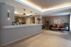 A modern reception area with a counter, seating, and a large potted plant. - Bomma House - Parque 93 (Bogotá)