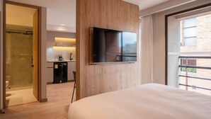 A modern hotel room with a large bed, a TV mounted on a wooden panel, a glass shower enclosure, and a kitchenette with a coffee machine. - Bomma House - Parque 93 (Bogotá)