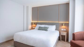 Una habitación de hotel moderna con una cama grande, dos mesitas de noche, una silla roja y un cabecero de madera.