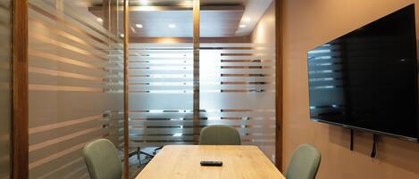 A conference room with a wooden table, two chairs, a remote control, and a mounted TV.