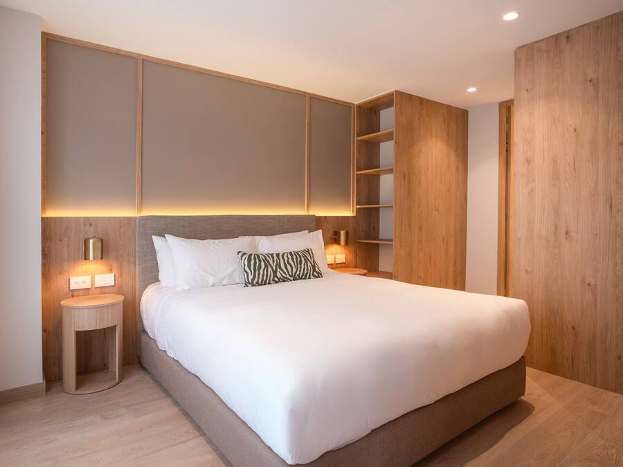 A modern bedroom with a large bed, wooden paneling, and built-in shelving.