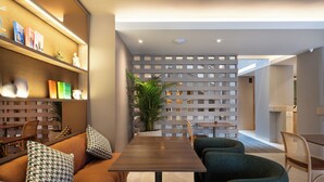 A modern interior with a wooden dining table, green upholstered chairs, a sofa with patterned cushions, and a decorative wall with shelves. - Bomma House - Parque 93 (Bogotá)