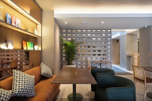 Un interior moderno con una mesa de comedor de madera, sillas tapizadas en verde, un sofá con cojines estampados y una pared decorativa con estantes.