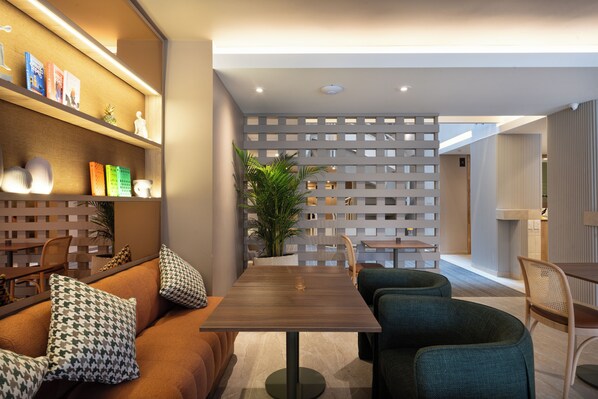 Un interior moderno con una mesa de comedor de madera, sillas tapizadas en verde, un sofá con cojines estampados y una pared decorativa con estantes.